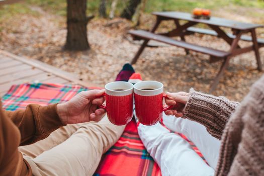 Hot cups of tea in hands in woollen sweater on background of cozy house