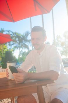 Young man in white shirt with smartphone in outdoor cafe
