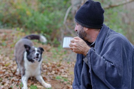 man drinking a cup of coffee with his dog in the background