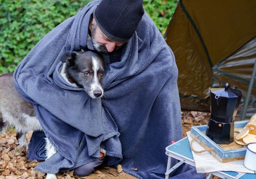 man camping covered with a blanket with his dog