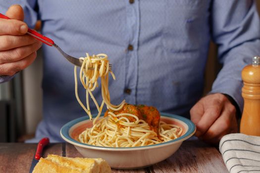 man with a fork eating meatballs with spaghetti