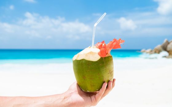 Coconut drink in palm hand on a tropical beach La Digue Seychelles Islands