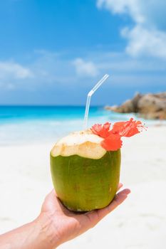 Coconut drink in palm hand on a tropical beach La Digue Seychelles Islands