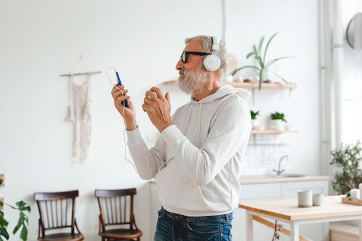 Happy senior man dancing while listening to music with headphones - active old people and enjoyment dance mood