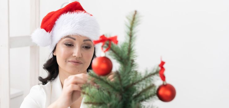 Banner smiling latin or indian business woman decorating christmas tree in office copy space. Happy middle eastern woman decorating tree for christmas holiday. Multiethnic people celebrating holiday at work.