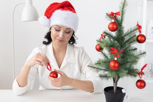 Portrait of smiling latin or indian business woman decorating christmas tree in office. Happy middle eastern woman decorating tree for christmas holiday. Multiethnic people celebrating holiday at work.