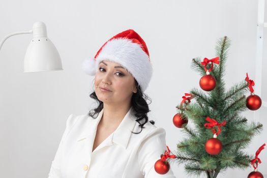 Portrait of smiling latin or indian business woman decorating christmas tree in office copy space. Happy middle eastern woman decorating tree for christmas holiday. Multiethnic people celebrating holiday at work.