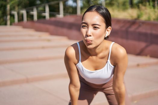 Portrait of sportswoman panting, taking break during jogging training, sweating while running outdoors