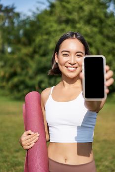 Vertical shot of fit and healthy young asian woman, shows smartphone screen with her workout stats, recommends telephone application