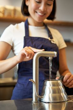 Vertical shot of girl barista in cafe pouring water from tap, using kettle to brew filter coffee