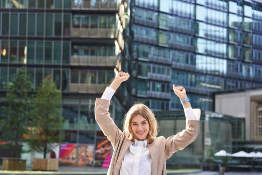 Corporate woman celebrating her victory outside on street. Happy businesswoman raising hands up and triumphing from excitement