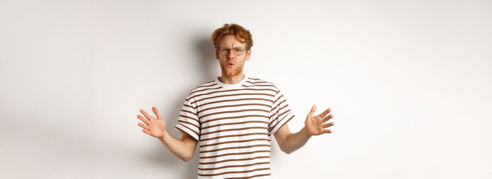 Impressed redhead man in glasses showing length of something big, demonstrate large size and looking amazed, standing over white background