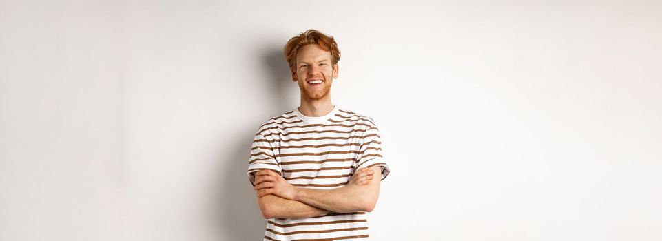 Happy redhead guy with bristle laughing and smiling at camera, standing with hands crossed on chest over white background