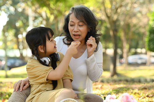 Happy middle aged woman and little granddaughter enjoying picnic in park together, spending leisure activity outdoor