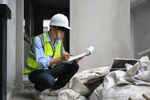 Image of inspector or engineer writing on clipboard, checking building material at construction site.
