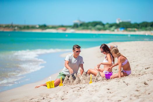 Parents and little daughter enjoying time on the beach. Family making sand castle together on the seashore