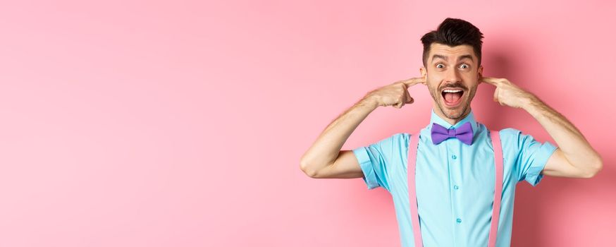 Childish funny guy shut ears and laughing at camera, refuse to listen, standing ignorant on pink background