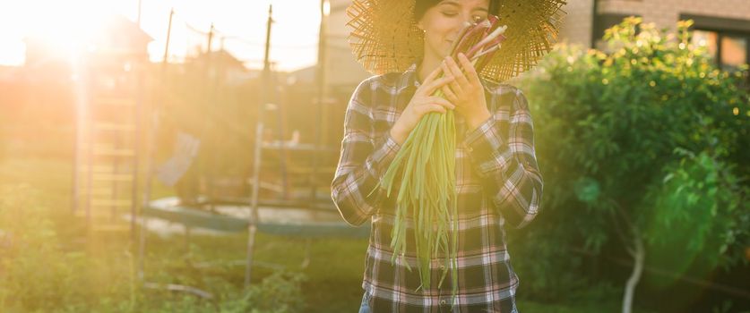 Banner female gardener sniffs bunch of green onions on sunny warm spring day copy space. Plant care and harvest concept and hobby