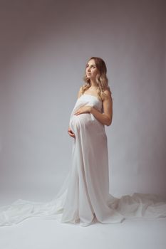 Elegant pregnant young woman standing wearing light fabric. Pregnancy, fantasy and fairy tale concept.
