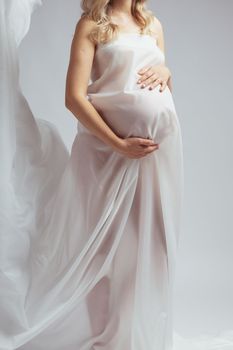 Close-up Elegant pregnant young woman standing wearing light fabric. Pregnancy, fantasy and fairy tale concept.