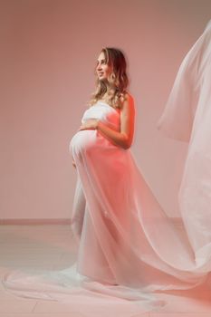 Elegant pregnant young woman standing wearing light fabric. Pregnancy, fantasy and fairy tale concept.