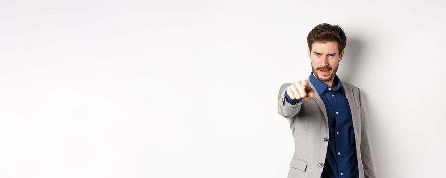 Confident and motivated businessman in suit need you, pointing finger at camera with encouraging face, choosing person, standing on white background