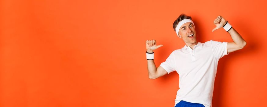 Concept of sport, fitness and lifestyle. Image of confident middle-aged man pointing at himself proudly, wearing clothes for workout, standing over orange background.