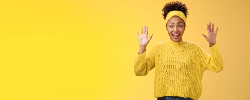 Charming excited smiling friendly millennial african-american girl raise hands nothing hide show palms high surrender standing amused thrilled grinning having fun posing yellow background