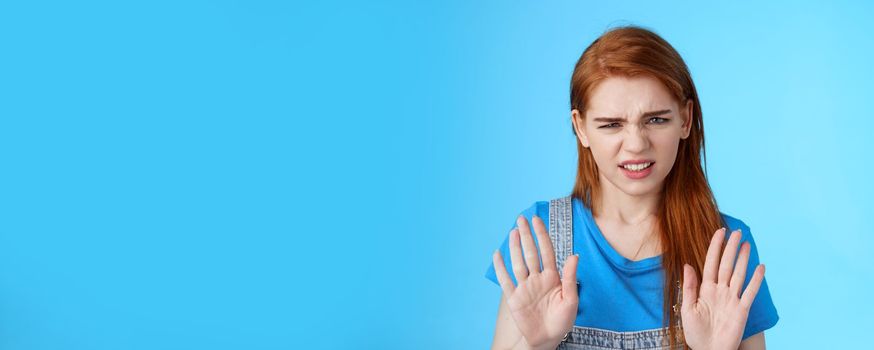 Close-up uninterested displeased ignorant picky redhead girlfriend, frowning make disgusted grimace raise hands block stop gesture, refuse, waving arms no rejection sign, stand blue background