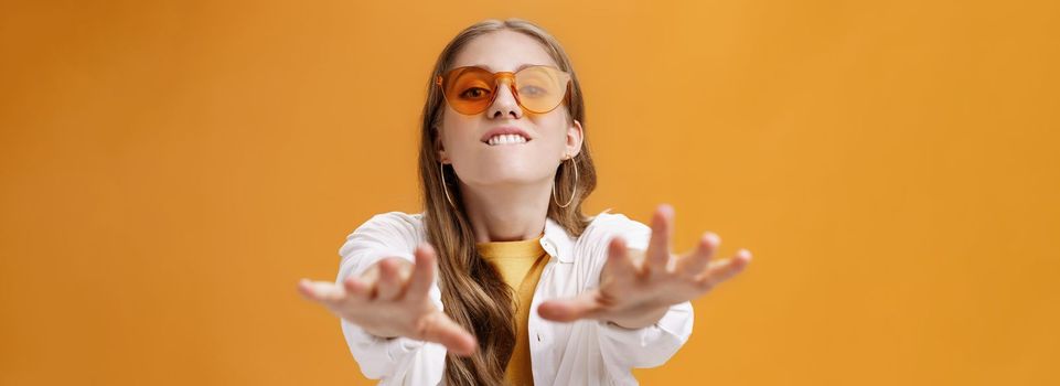 Girl reaching with desire at camera wanting grab it. Portrait of good-looking stylish caucasian young woman in trendy sunglasses biting lip from will to have something pulling hands towards