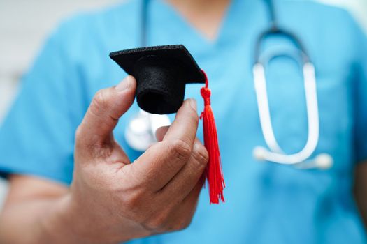 Asian woman doctor holding graduation hat in hospital, Medical education concept.