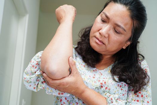 Asian senior woman wearing elastic support elbow brace for reduce pain.