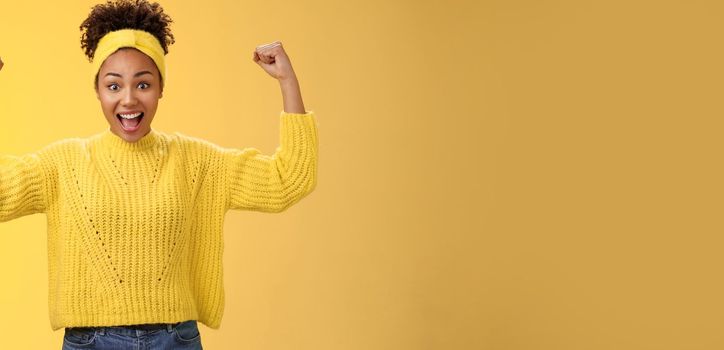 Proud impressed charming girlfriend encourage girlfriend win first place happy for friend rase fists celebration triumph gesture smiling broadly congratulation good work win, yellow background
