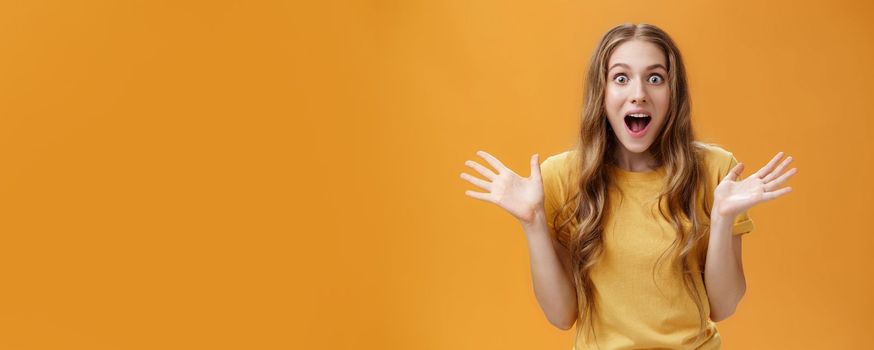 Impressed excited girl describing feelings sharing positive impression gesturing with palms during talk open mouth from amazement and oy communicating lively over orange background