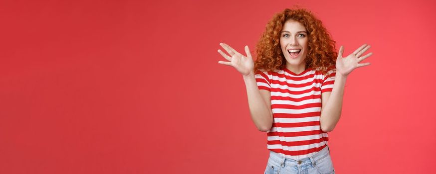 Awesome incredible performance bravo. Attractive cheerful cute european redhead curly female raise hands thrilled express excitement happiness joy look camera entertained delighted red background
