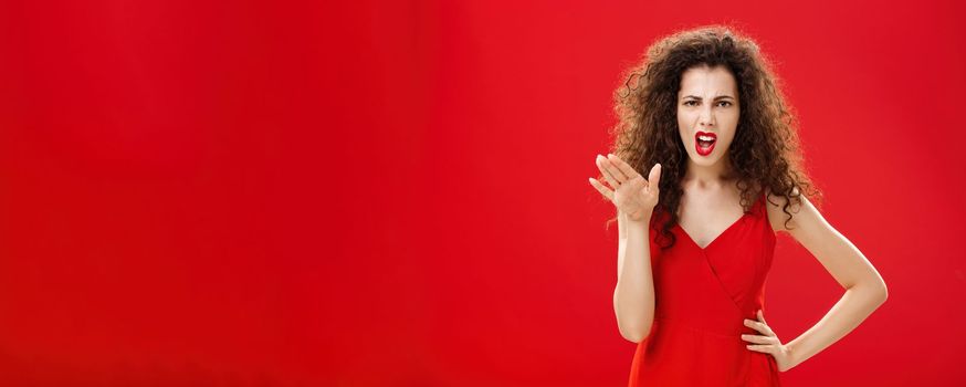 Girl chowing her temper to employees being fed up with unappropriate behaviour complaining standing pissed and dissatisfied gesturing with palm and holding hand on hip over red background