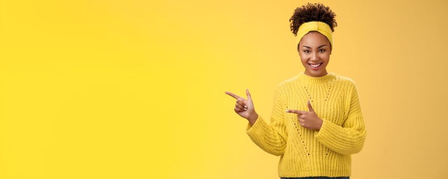 Confident good-looking millennial feminine african-american woman headband sweater look self-assured assertive pointing left index fingers you gonna like it smile, standing yellow background