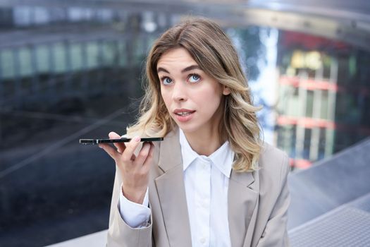 Young office girl talking on mobile phone, recording voice message, holding smartphone near mouth