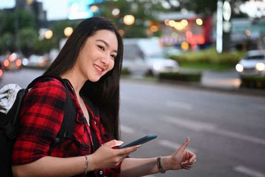 Cheerful young woman using application of taxi service app on smart phone in the city at night.