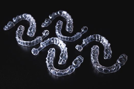 pattern of transparent aligners, invisible braces lies on a black background. No people