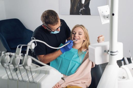 Portrait of a dentist in eyeglasses who treats teeth of young blond woman patient.