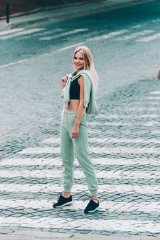 Stylish beautiful young blond woman in a light green tracksuit posing on the street. Attractive girl model posing outdoors