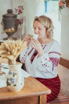 Beautiful peasant Ukrainian woman drinks tea in an old Ukrainian hut