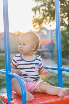 Blonde baby sitting on a swing at sunset