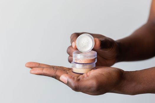 African american man holds mineral facial powder for perfect make-up for women - male make-up artist and cosmetic product concept
