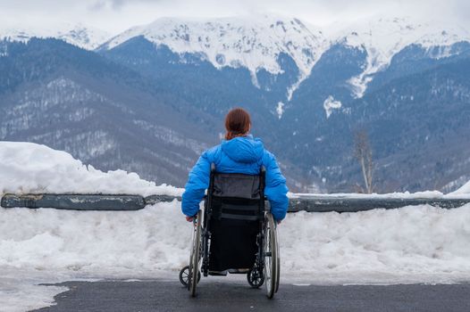 Rear view of a woman in a wheelchair travels in the mountains in winter.