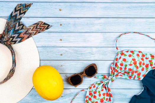 Top view of a straw white hat with glasses and a swimsuit, lying on a blue wooden background.Summer vacation concept