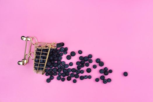 Blueberries in a grocery cart on a pink background. Scattered blueberries near a grocery cart on a pink background.