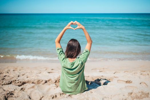 Young beautiful woman on the beach vacation looking at the sea and making heart by hand