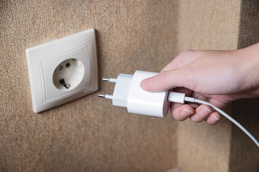 Hand turns on, turns off charger in electrical outlet on wall, close-up with